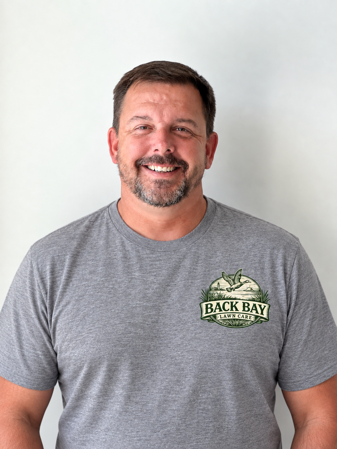 Patrick Davis, owner of Back Bay Lawn Care, wearing a gray shirt with the company logo